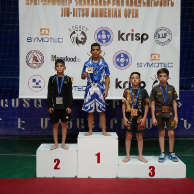Young Armenian athlete Mark Ghambaryan standing proudly on the podium after winning gold at the Jiu-Jitsu Armenian Open Championship in Honor of Garik Arevikyan